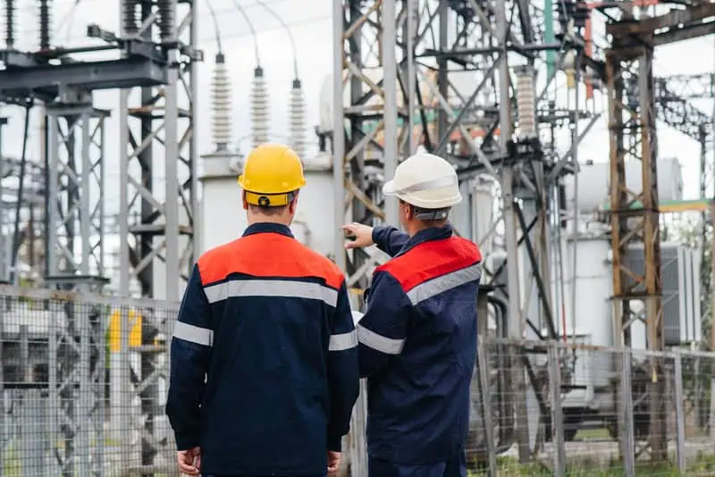 Engineers inspecting electrical substation equipment outdoors.